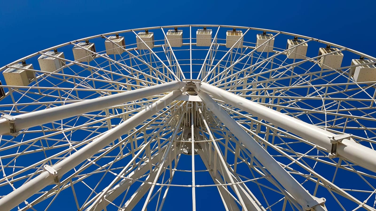 Big white ferris wheel against the blue sky. Part of the attraction on a blue background with copy space. Cabins, viewing platforms