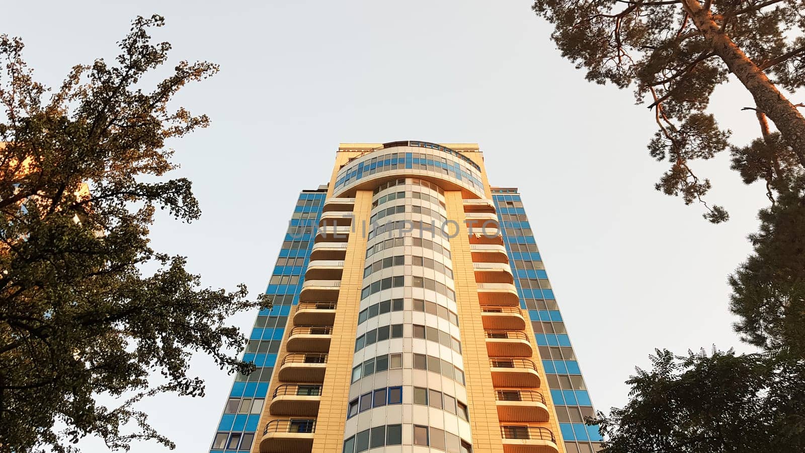 Ukraine, Kiev - May 25, 2020: modern multi-storey residential building against the blue sky and green trees. Exterior wall of a colorful residential new building. View from below