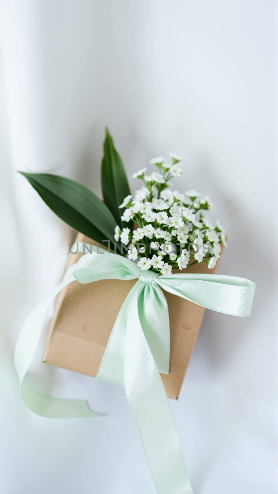 The gift comes in minimalist packaging, decorated with a neutral, calm blue ribbon and flowers symbolizing the arrival of spring. High quality photo