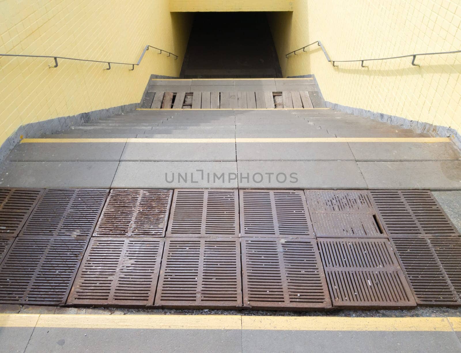 Empty yellow underground pedestrian crossing. Tunnel and daylight at the end. Steps to the top at the pedestrian crossing. A long concrete tunnel with lanterns in the city underground