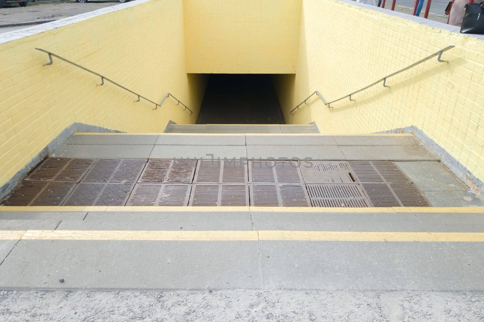 Empty yellow underground pedestrian crossing. Tunnel and daylight at the end. Steps to the top at the pedestrian crossing. A long concrete tunnel with lanterns in the city underground
