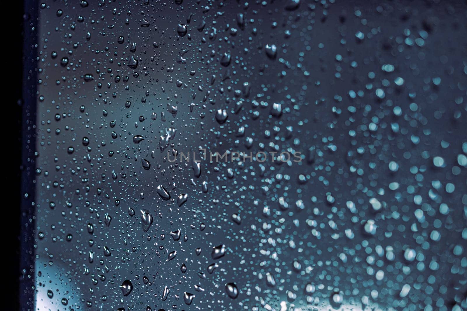 Close up of rain drops on the window in rainy night, cool lights and window frame