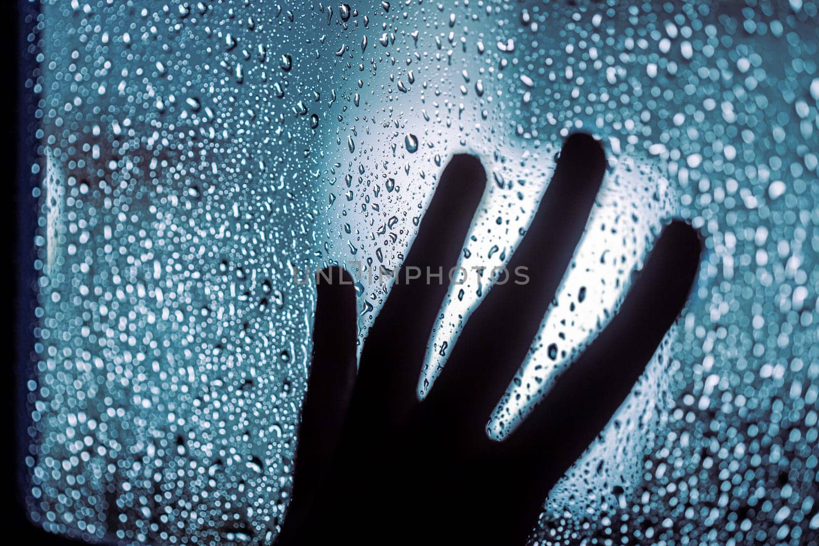 Close up of hand silhouette on window with water drops, night