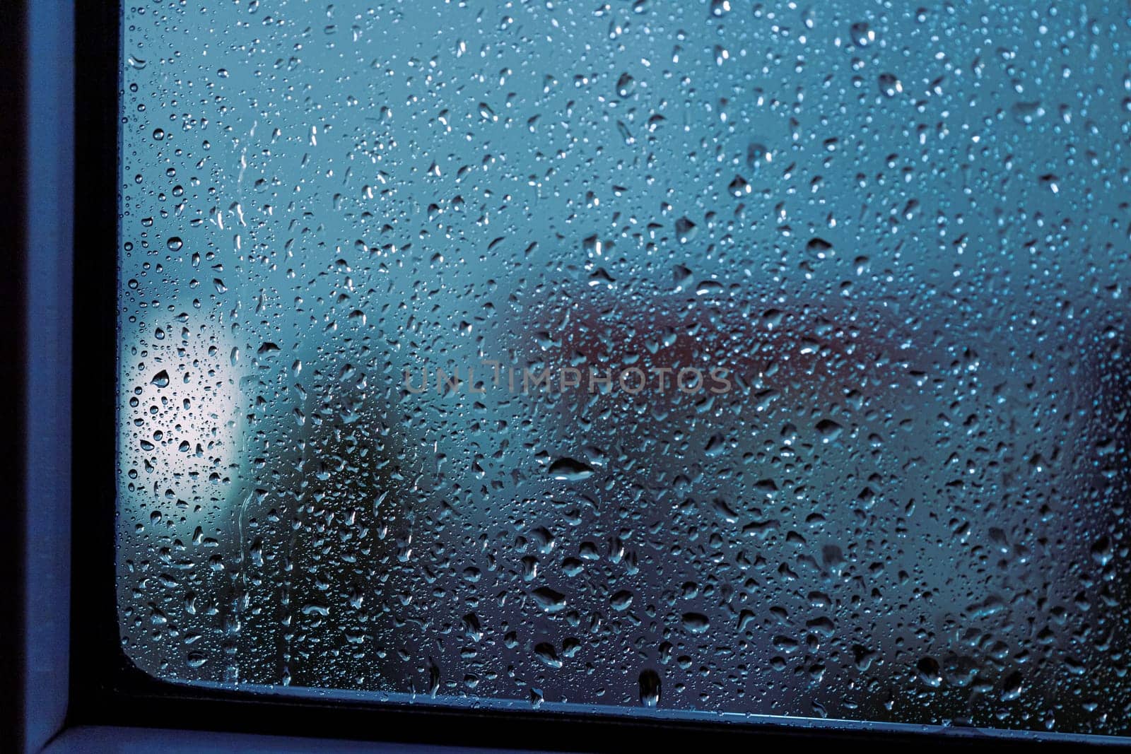 Close up of rain drops on the window in rainy night, cool lights and window frame