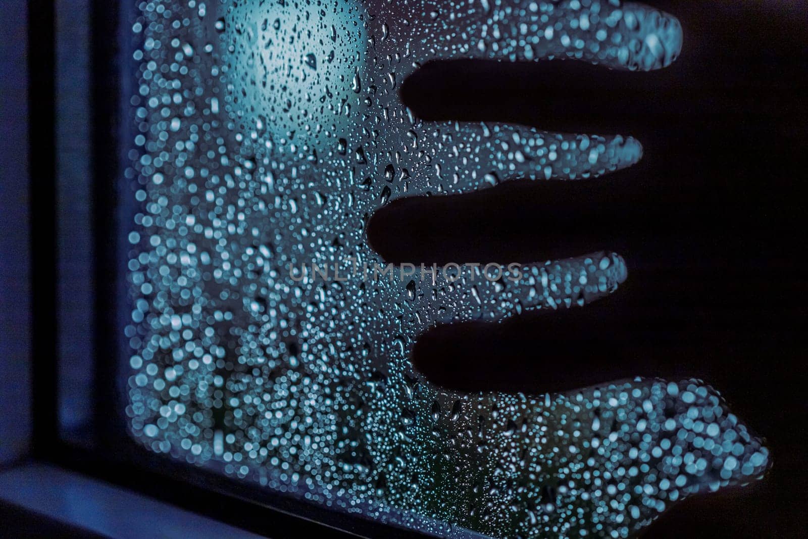 Close up of hand silhouette on window with water drops, night