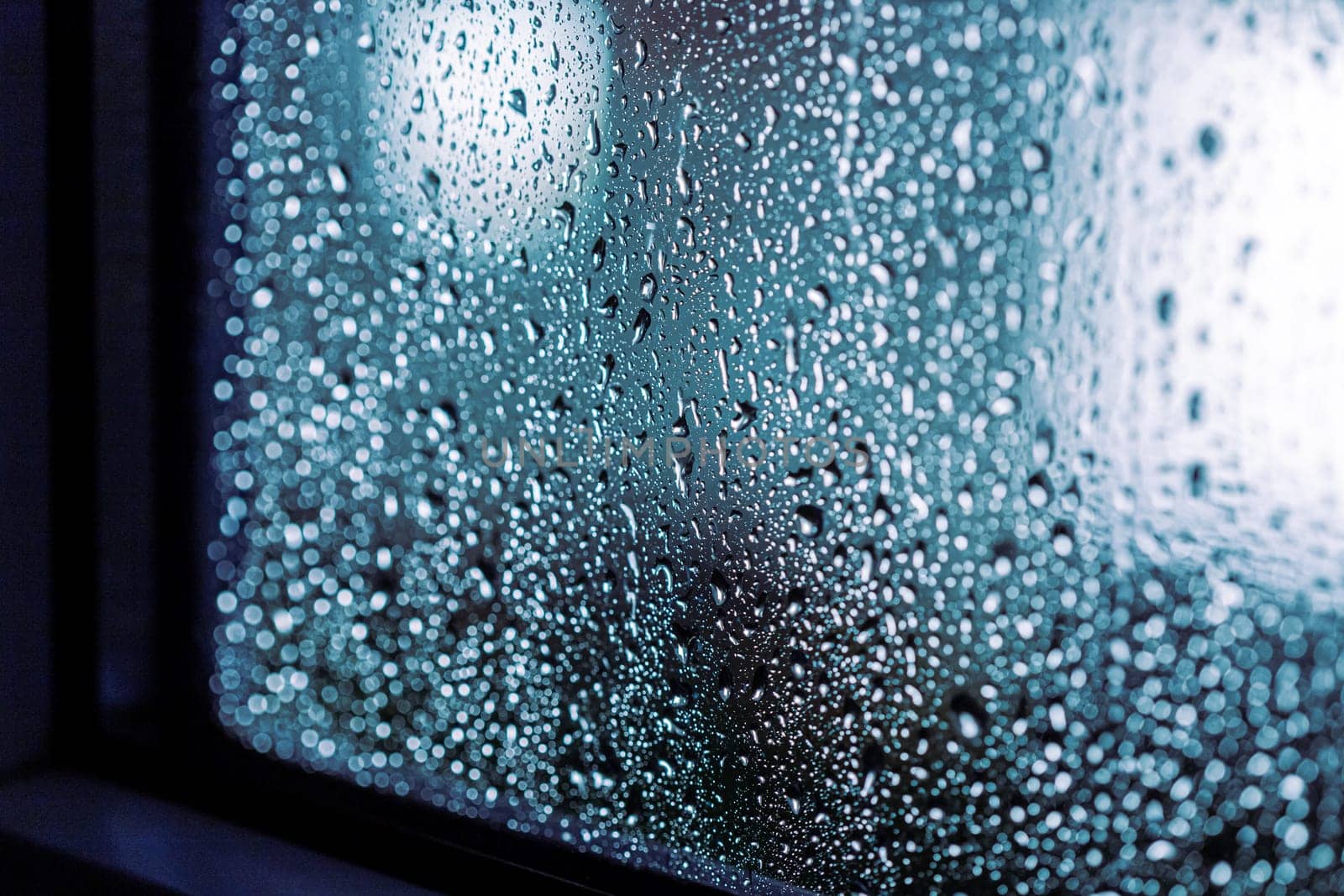 Close up of rain drops on the window in rainy night, cool lights and window frame