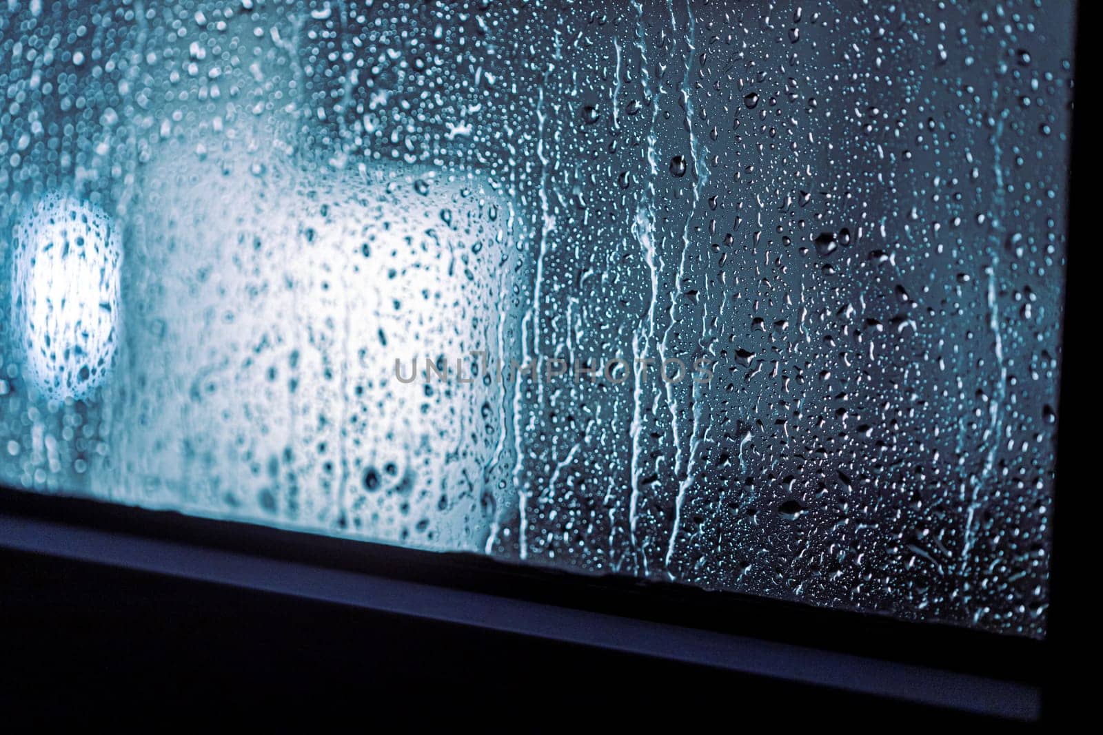 Close up of rain drops on the window in rainy night, cool lights and window frame