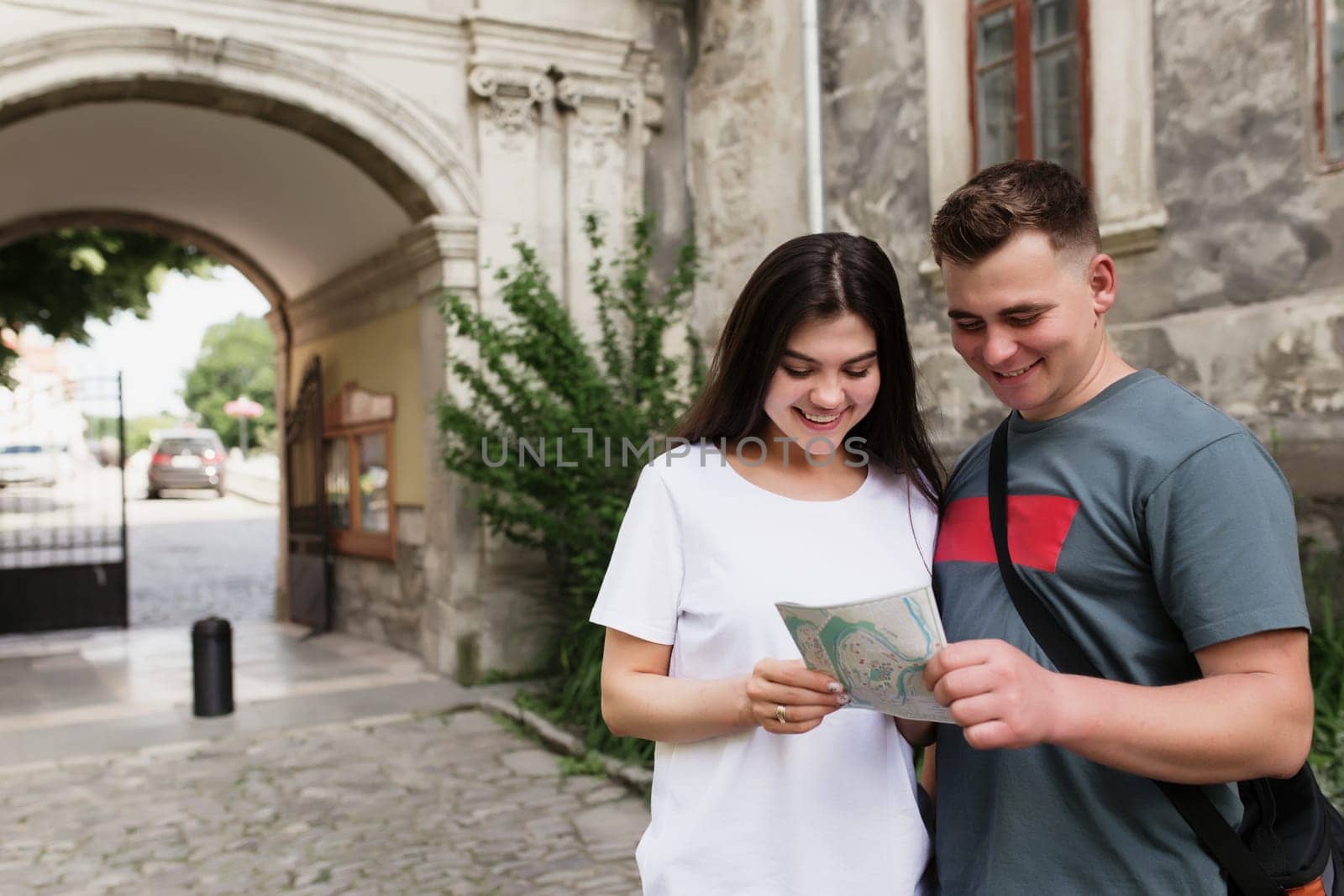 A couple of handsome heterosexual tourists in love looking at a city map to understand how to find a place. The girl points her finger and smiles. Wife and husband have a vacation trip to other city.