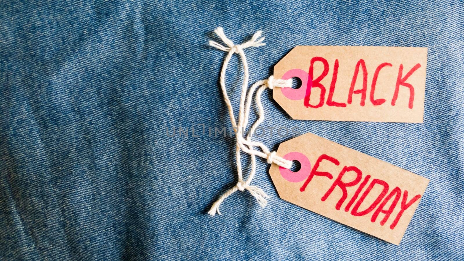 Stylish jeans with a black friday flag. Black friday and cyber monday sale discount concept tag with blue jeans. Black friday written on grunge jeans texture. Background, holiday concept. Black Friday - International day of shopping, promotions, discounts, sales. The sales season is the fourth Thursday of November. Copy space, place for text, flat lay.