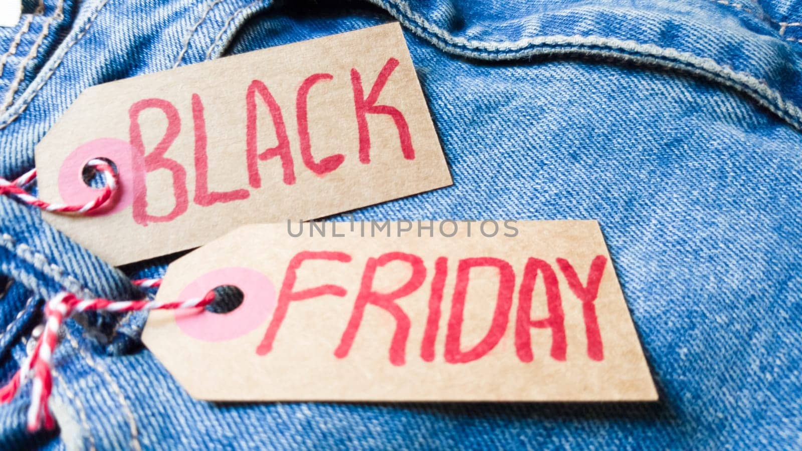 Stylish jeans with a black friday flag. Black friday and cyber monday sale discount concept tag with blue jeans. Black friday written on grunge jeans texture. Background, holiday concept. Black Friday - International day of shopping, promotions, discounts, sales. The sales season is the fourth Thursday of November. Copy space, place for text, flat lay.