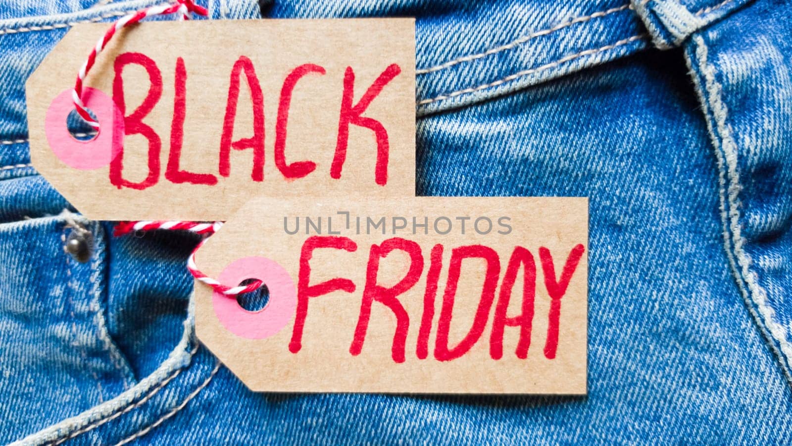 Stylish jeans with a black friday flag. Black friday and cyber monday sale discount concept tag with blue jeans. Black friday written on grunge jeans texture. Background, holiday concept. Black Friday - International day of shopping, promotions, discounts, sales. The sales season is the fourth Thursday of November. Copy space, place for text, flat lay.