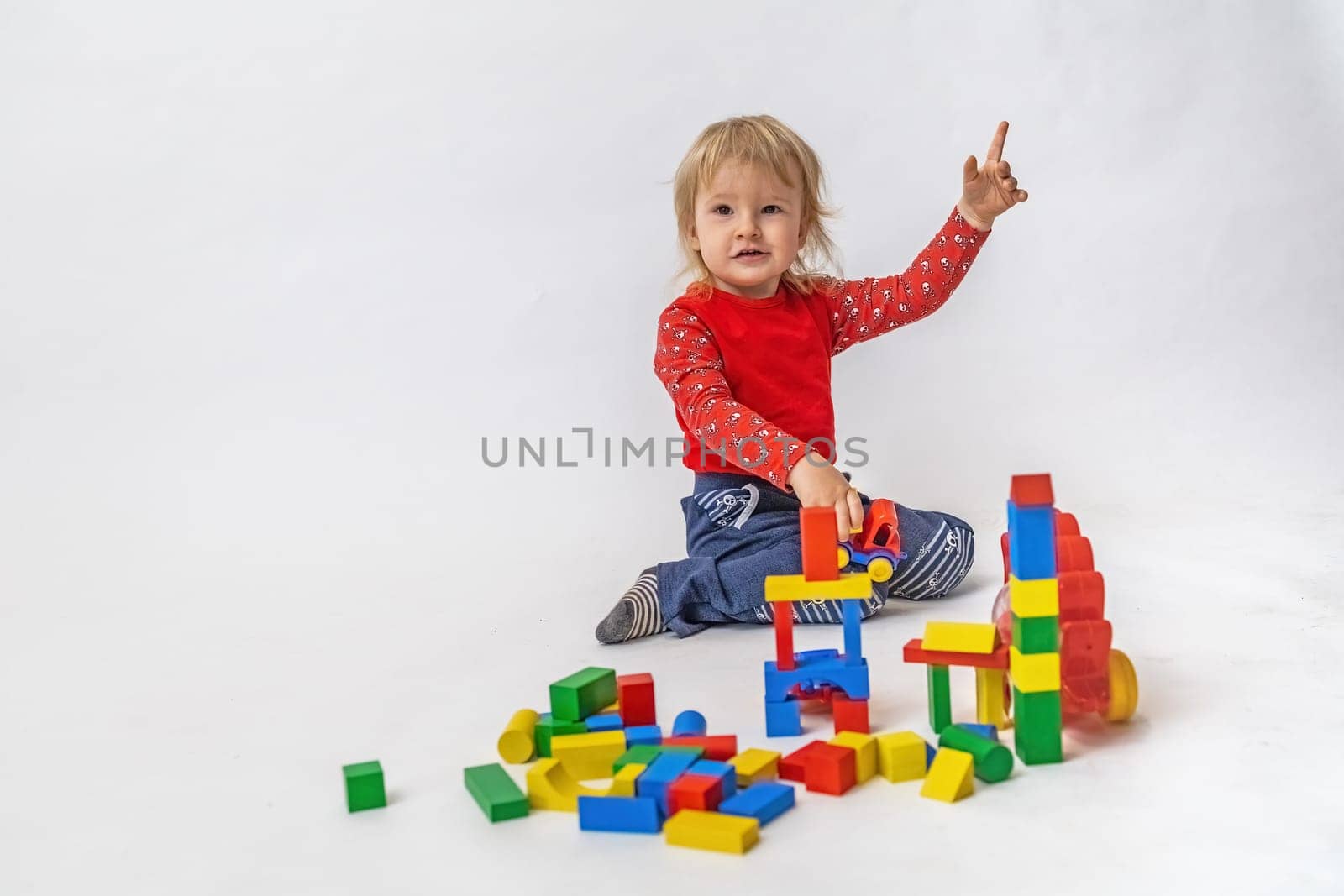 Cute little boy with his hand raised is playing with colorful wooden cubes. Horizontally.