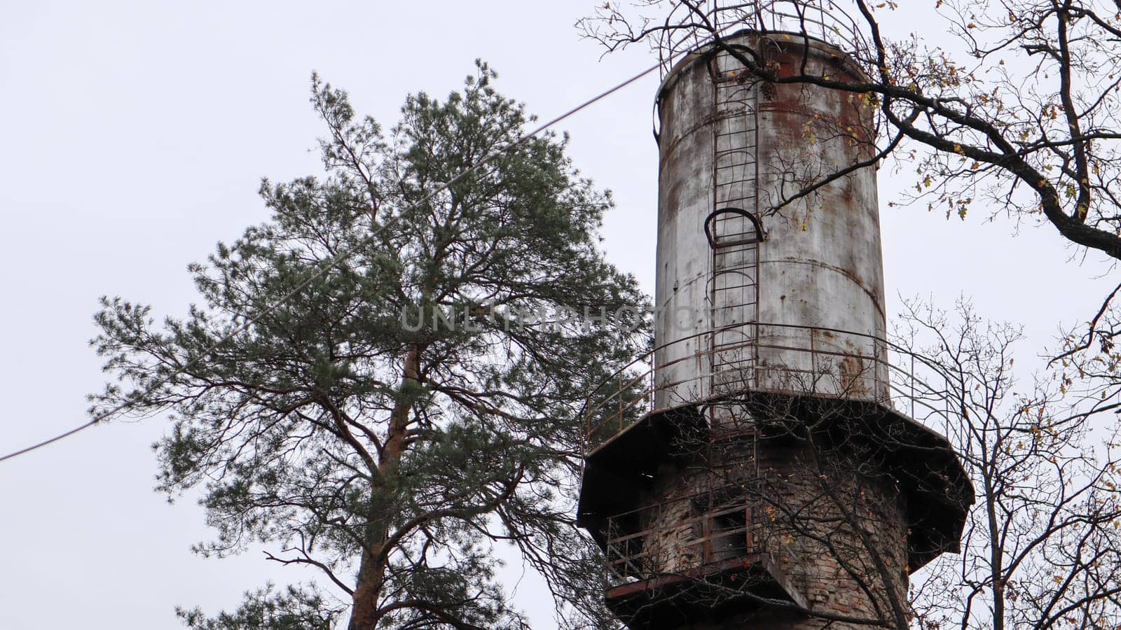 The pipe of the plant rise above the forest. Industrial landscape. Ecological production without smoke from pipes. Water tower in the village. Water supply to houses under a pressure. Rural landscape
