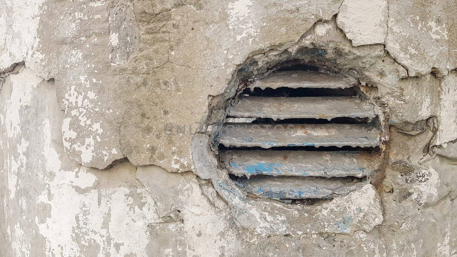 ventilation hole in concrete. Metal industrial round ventilation cover. Rusty and dirty old round ventilation frame with horizontal metal stripes