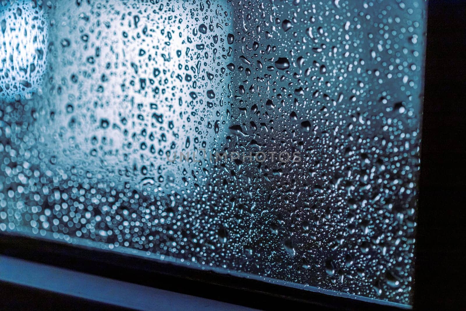Close up of rain drops on the window in rainy night, cool lights and window frame