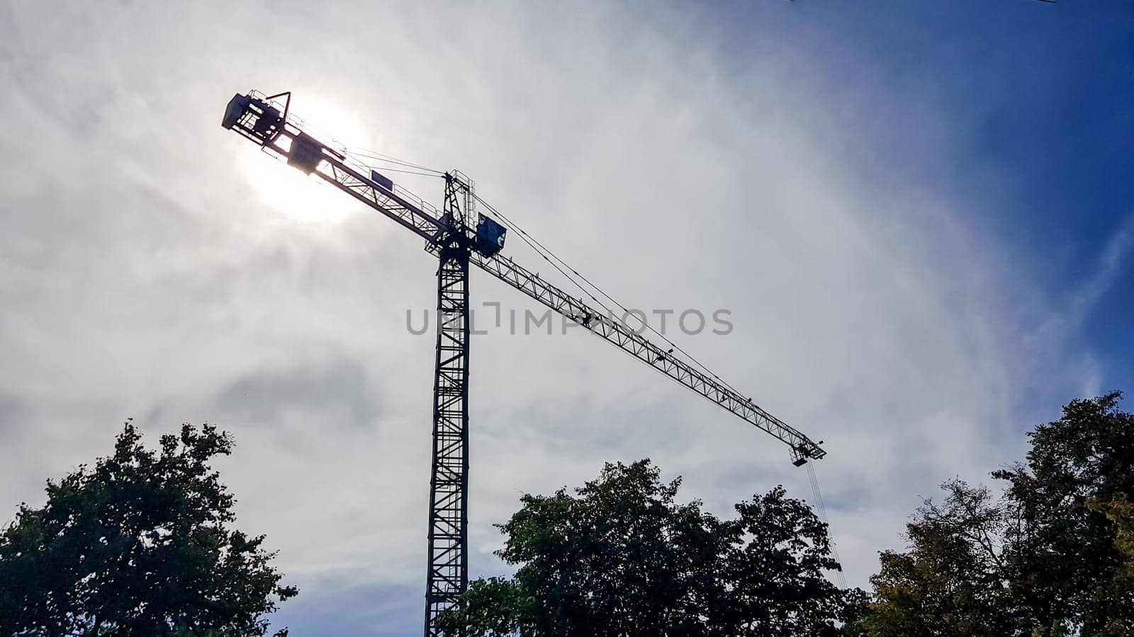 Construction crane on a background of blue sky. Close view of a construction crane. Abstract industrial background with a silhouette of a construction crane over the sky with clouds