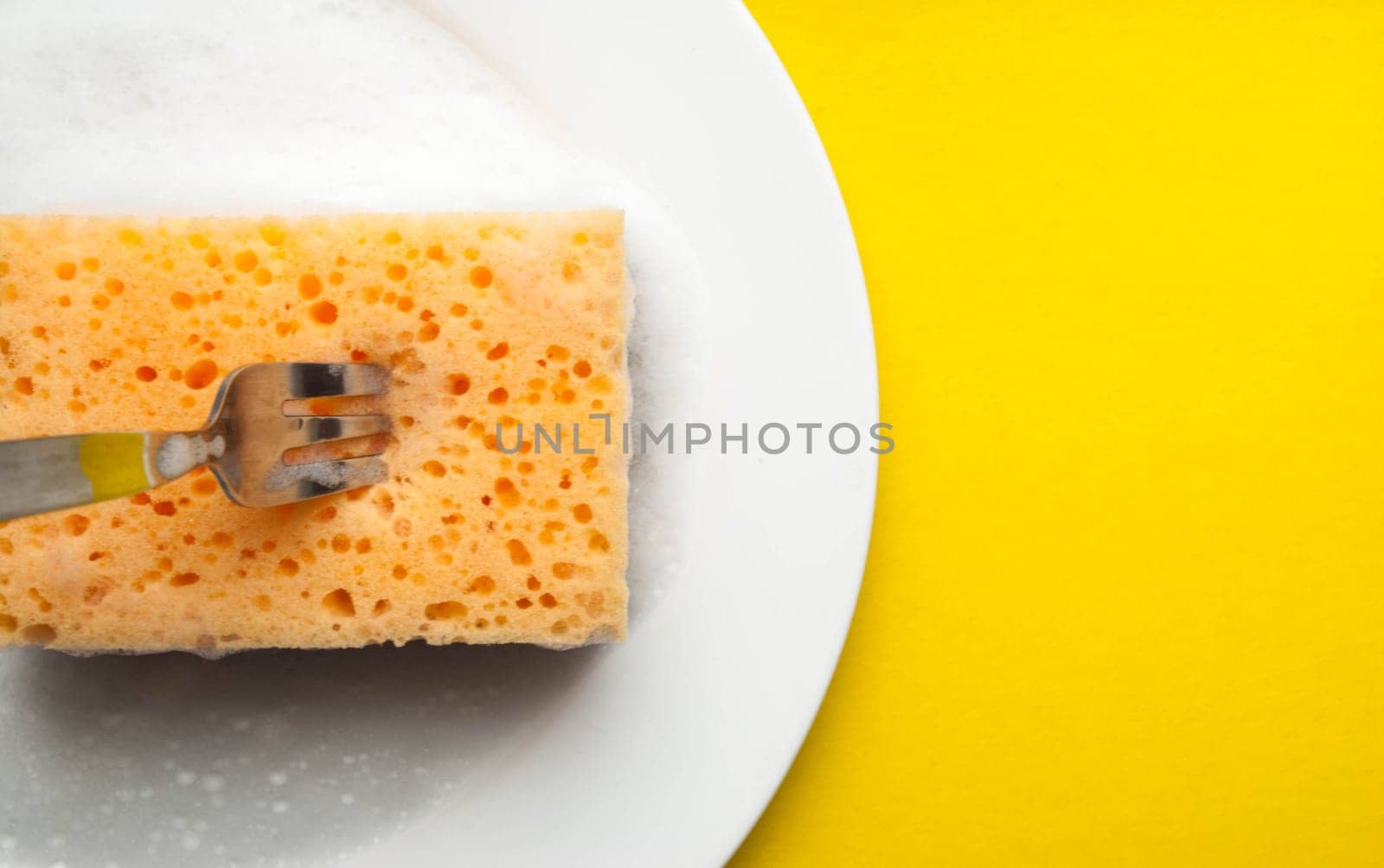 Cleaning sponge on a white plate on a yellow background.