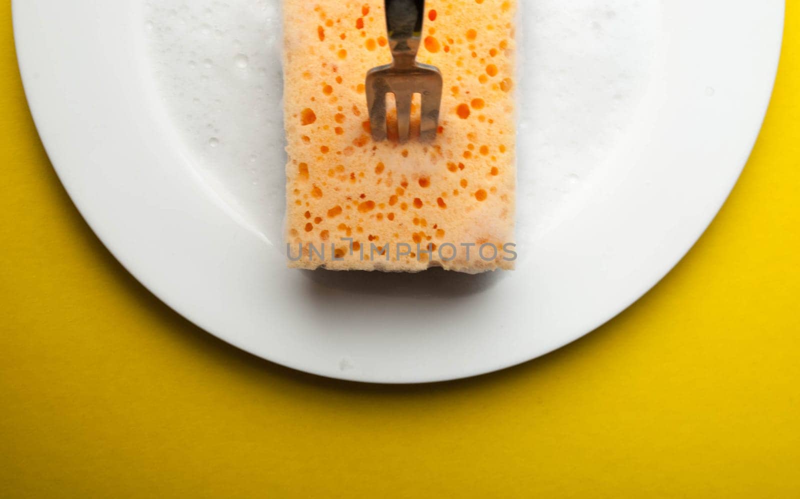 Cleaning sponge on a white plate on a yellow background.