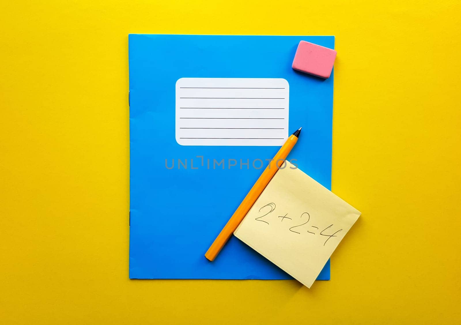 Blue notebook and textbook copy butt for school subjects, eraser, pencil, paper clip on a yellow background. The solution to the mathematical problem is written in pencil. Flat lay, copy space, top view, place for text