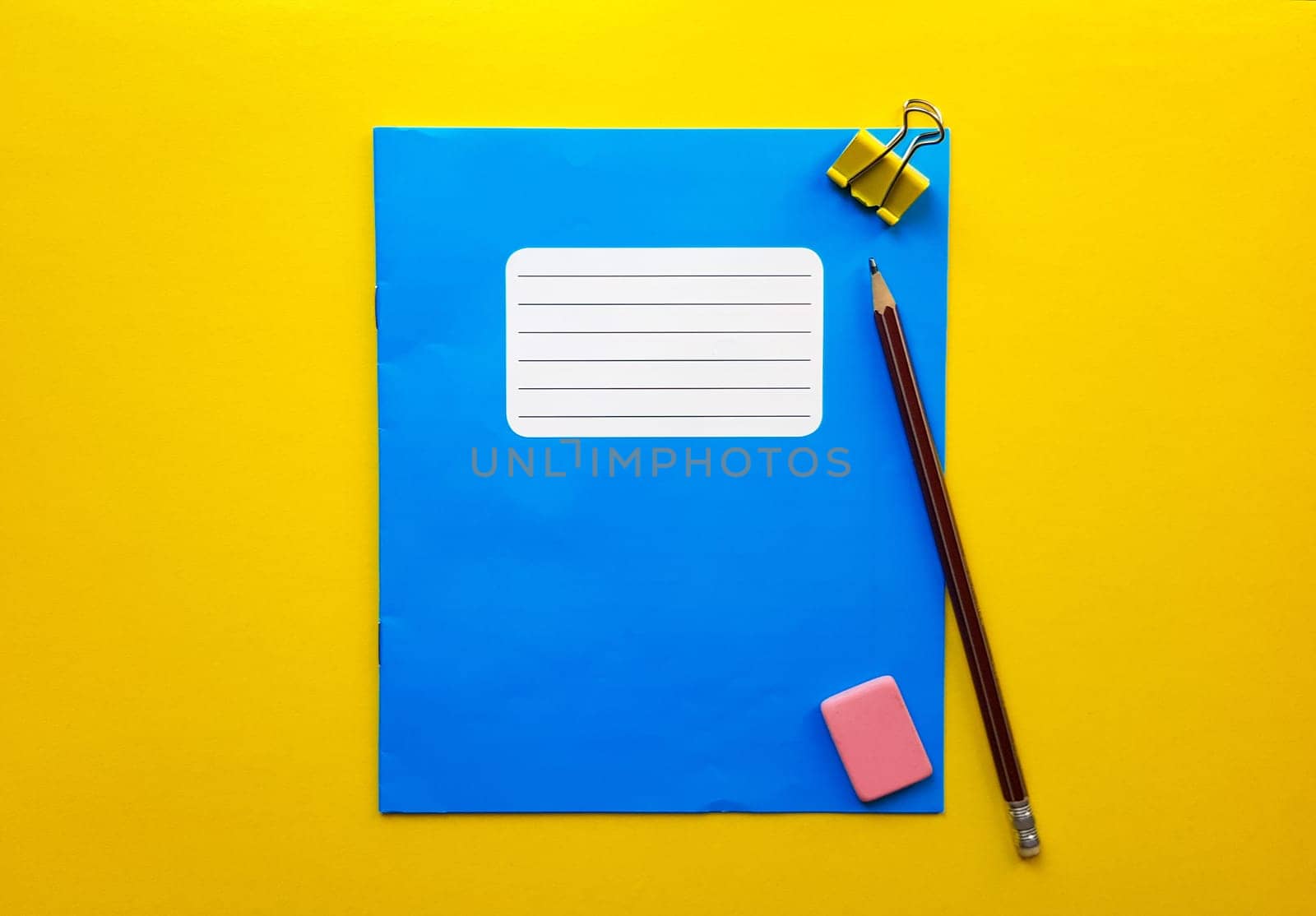 Blue mock up notebook and textbook butt for school subjects, eraser, pencil, paper clip on a yellow background. Flat lay, copy space, top view, place for text