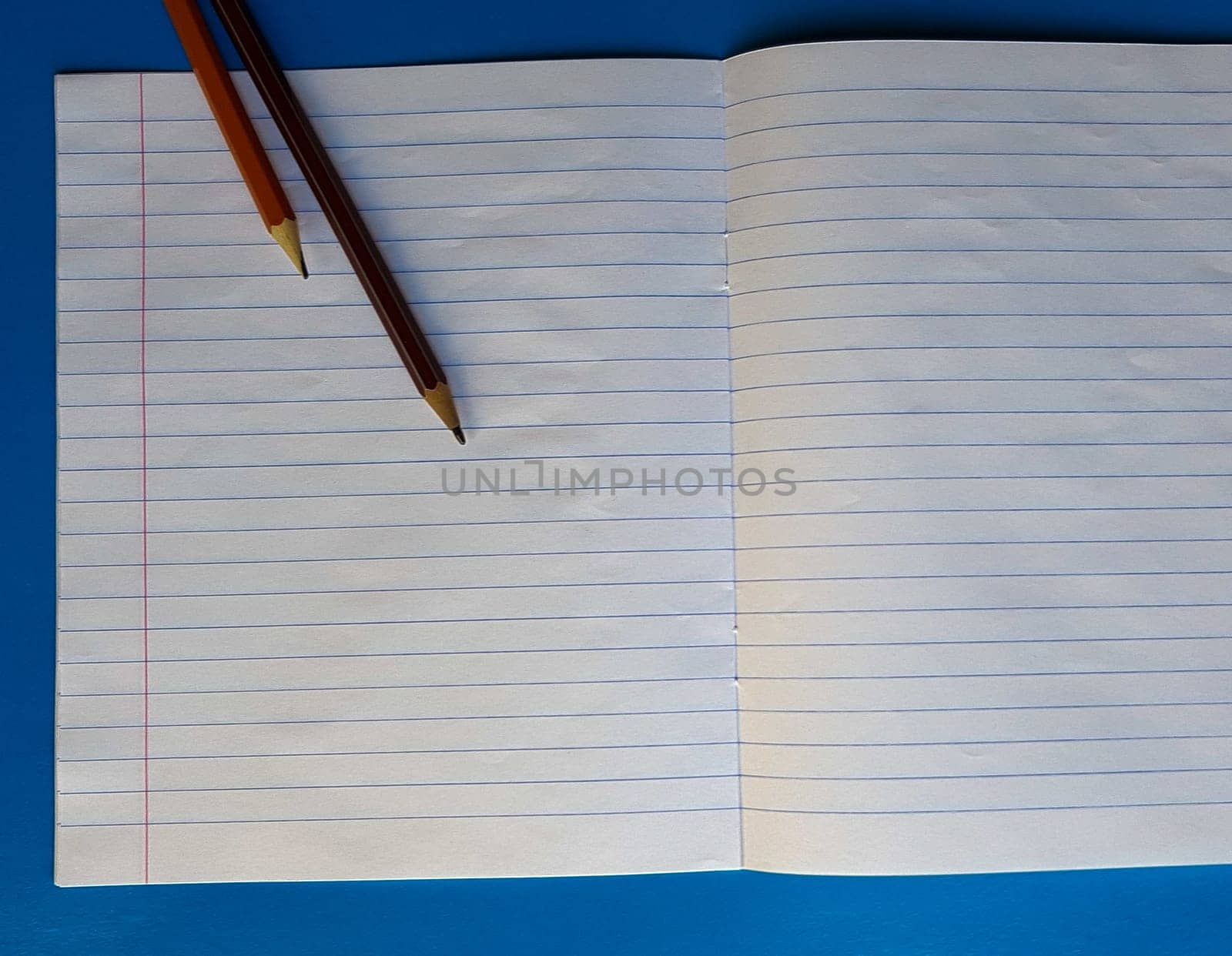 Open notebook on a white lining on a blue wooden tabletop with a pencil.