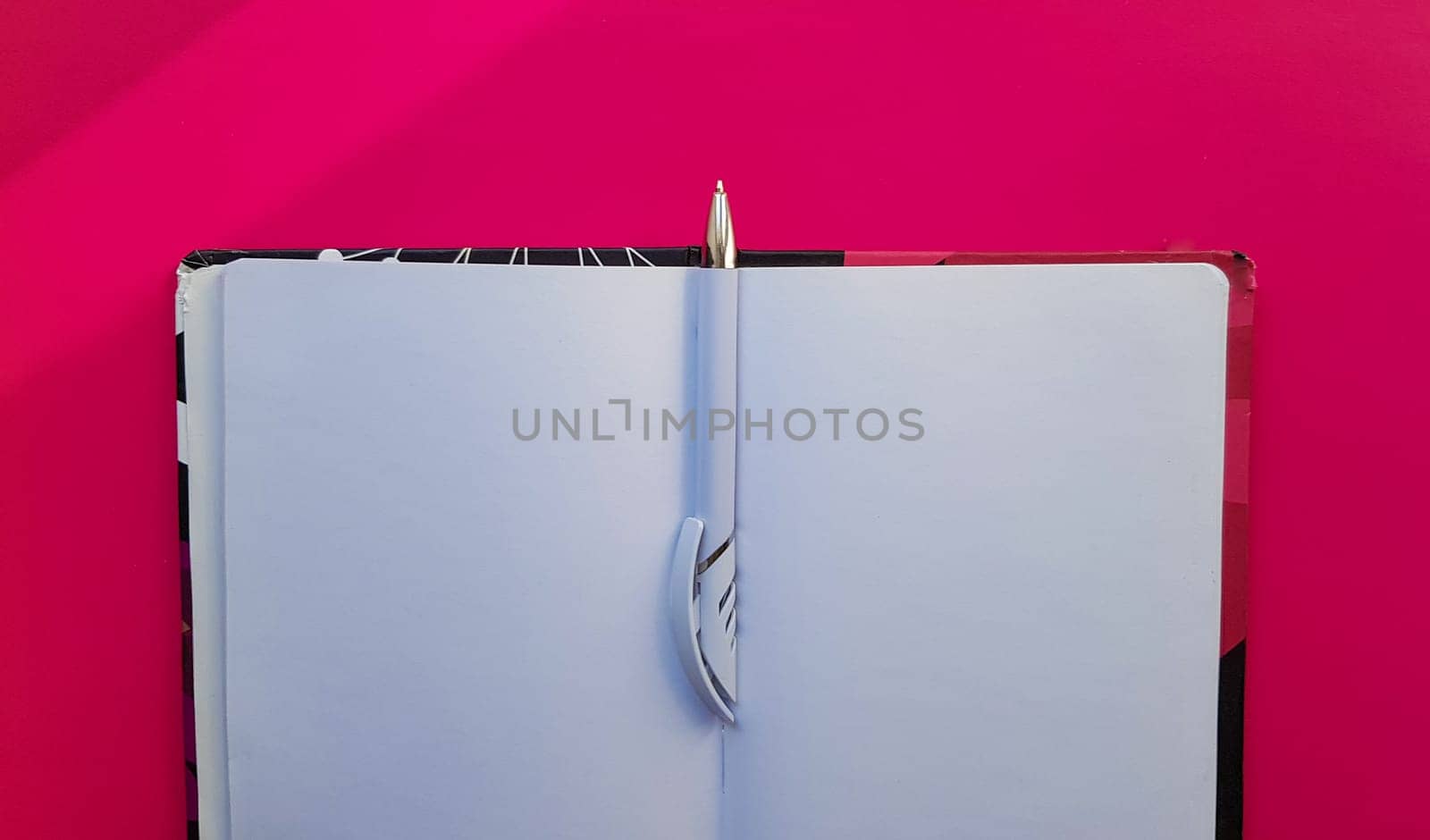 Blank notebook with white pen on a red background. Empty pages of an open book, space for writing and text. View from above. Copy space, flat lay.