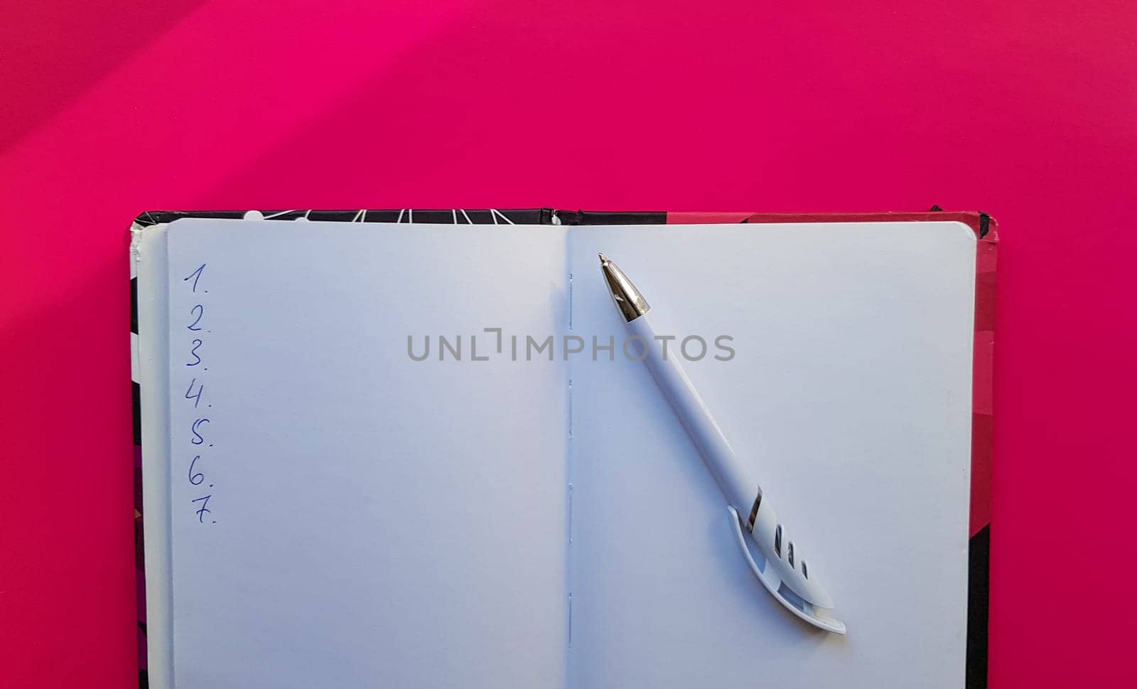 Blank notebook with white pen on a red background. Empty pages of an open book, space for writing and text. View from above. Copy space, flat lay.