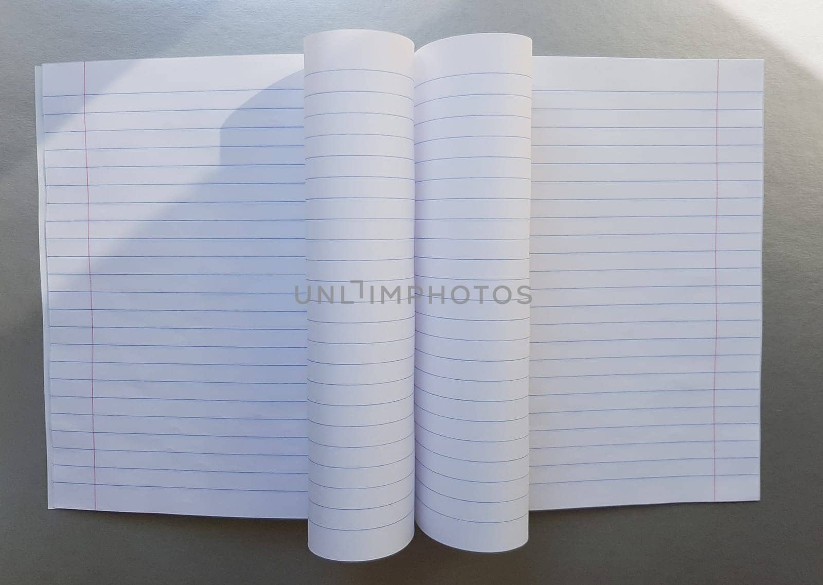 open school notebook with pen on a gray desk with sun rays from the window. A blank, white sheet of notebook for writing. education concept. Copy space. view from above. Flat lay.