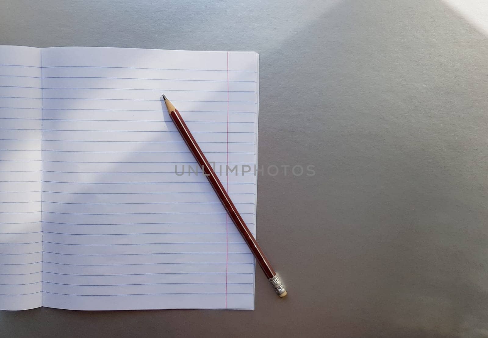 open school notebook with pen on a gray desk with sun rays from the window. A blank, white sheet of notebook for writing. education concept. Copy space. view from above. Flat lay.