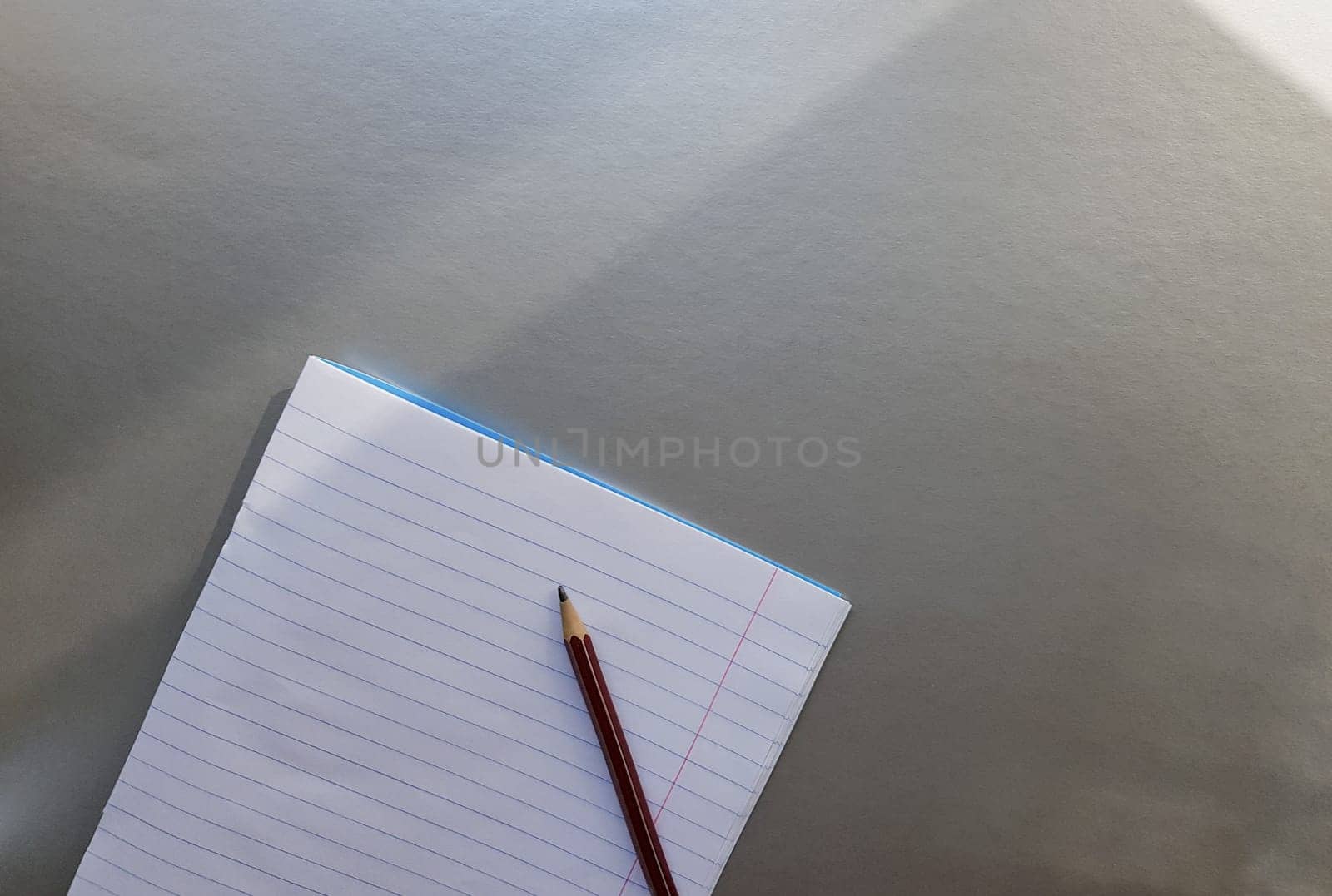 open school notebook with pen on a gray desk with sun rays from the window. A blank, white sheet of notebook for writing. education concept. Copy space. view from above. Flat lay.