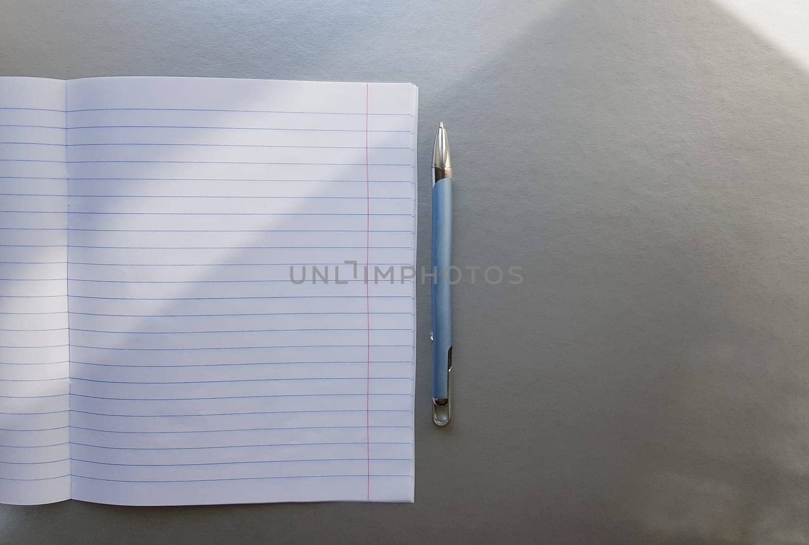 open school notebook with pen on a gray desk with sun rays from the window. A blank, white sheet of notebook for writing. education concept. Copy space. view from above. Flat lay.