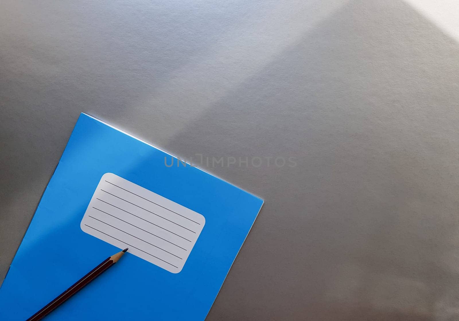 New blue notebook with pencil on a gray table with sun rays from the window background.