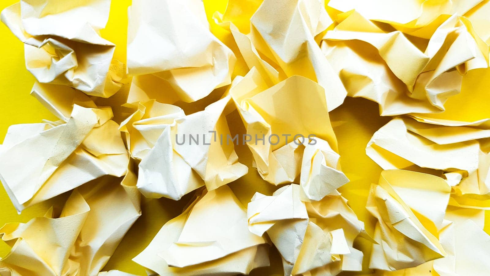 Ball crumpled paper ball isolated on a yellow background. Crumpled paper for texture. Crumpled paper after a brainstorming was thrown into the bin. A piece of yellow crumpled paper on a yellow background