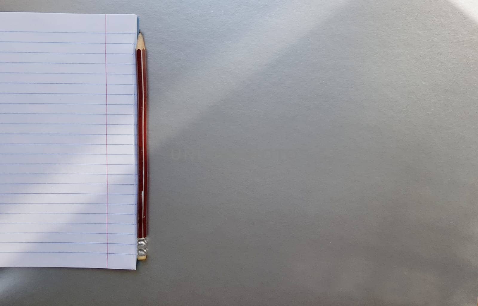 open school notebook with pen on a gray desk with sun rays from the window. A blank, white sheet of notebook for writing. education concept. Copy space. view from above. Flat lay.