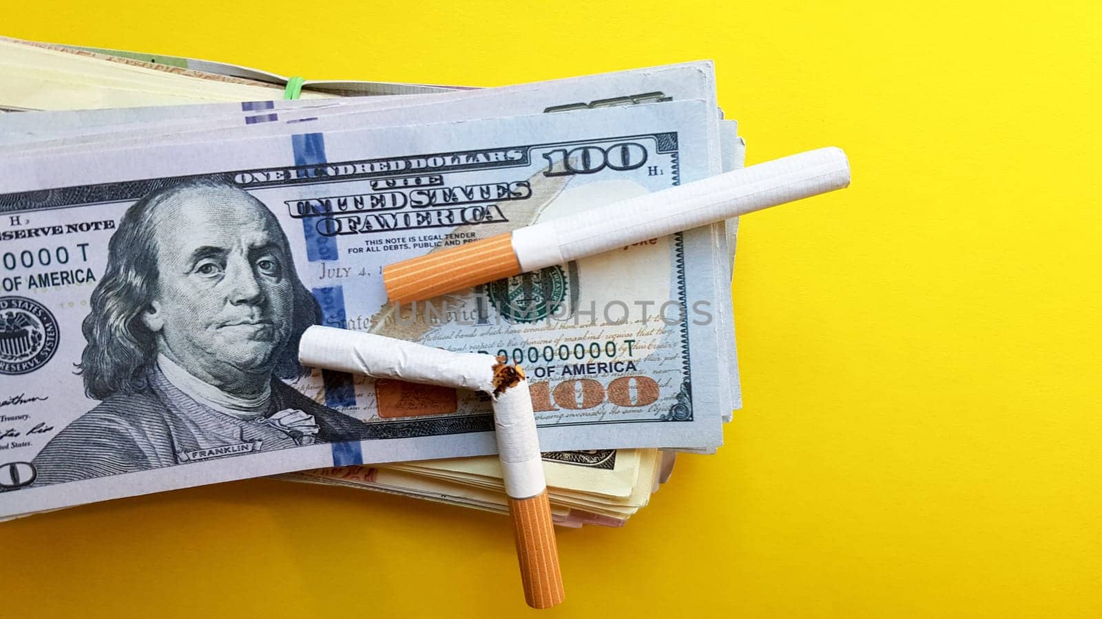 Classic cigarettes stand on one hundred US dollar bills. Cigarettes on a hundred dollar bill on a yellow background.