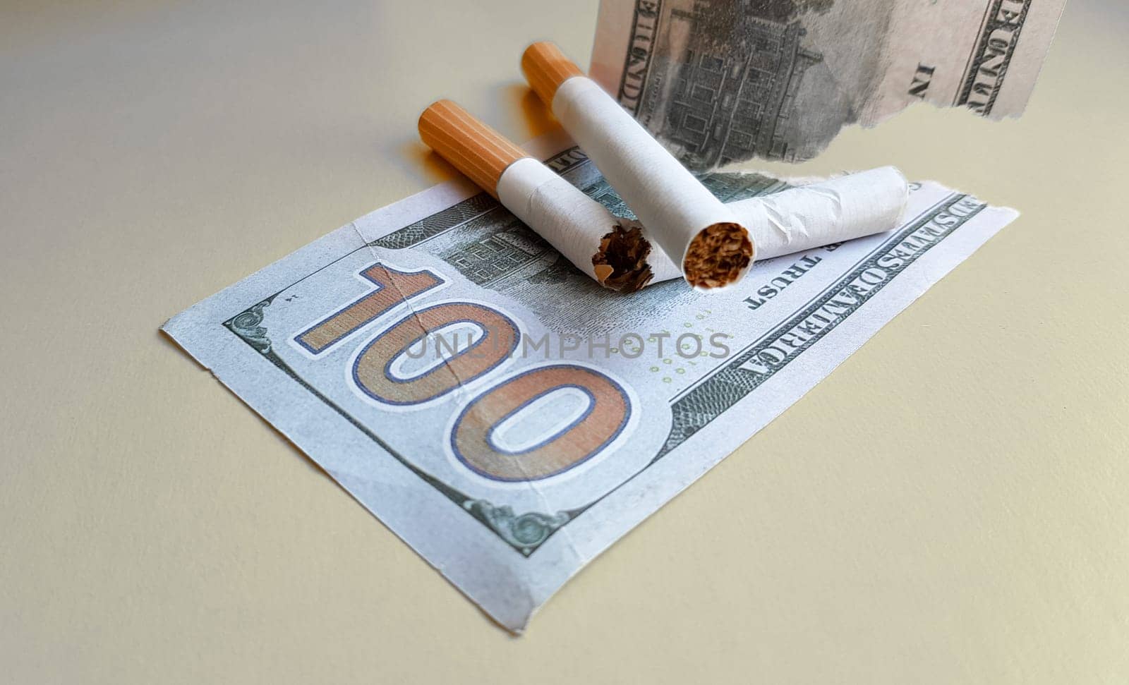 Classic cigarettes stand on one hundred US dollar bills. Cigarettes on a hundred dollar bill on a yellow background.