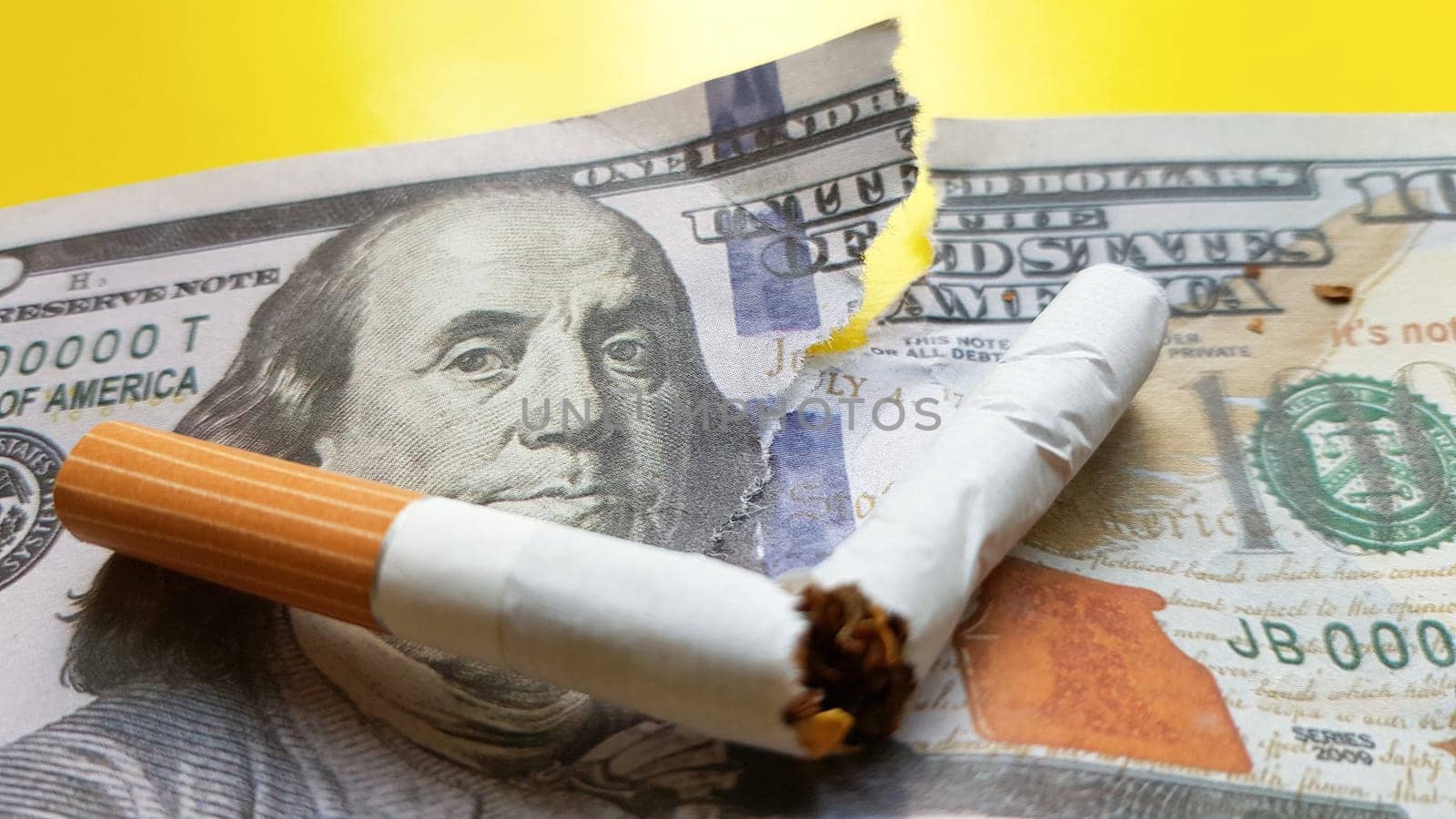 Classic cigarettes stand on one hundred US dollar bills. Cigarettes on a hundred dollar bill on a yellow background.