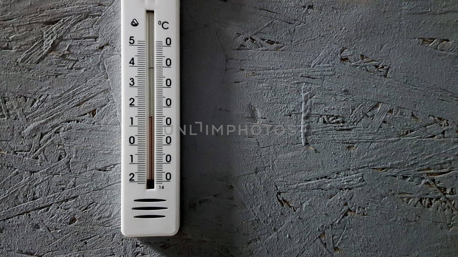 white thermometer hanging on a gray gray wooden wall indoors, background with copy space and empty place for your text.