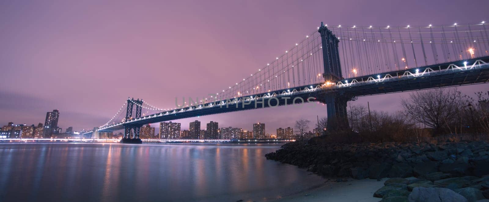 Manhattan bridge and New York City downtown skyline at dusk with skyscrapers illuminated over East River panorama. Copy space.