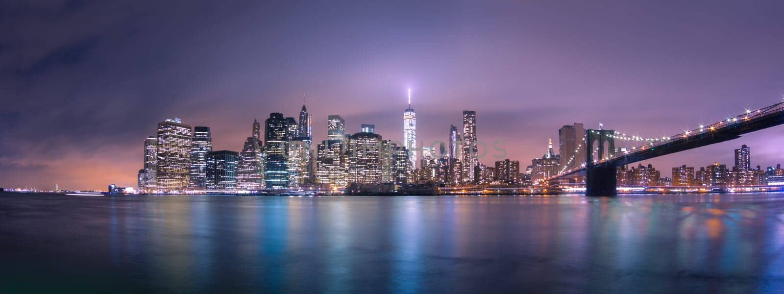 Manhattan bridge and New York City downtown skyline at dusk with skyscrapers illuminated over East River panorama. Copy space.