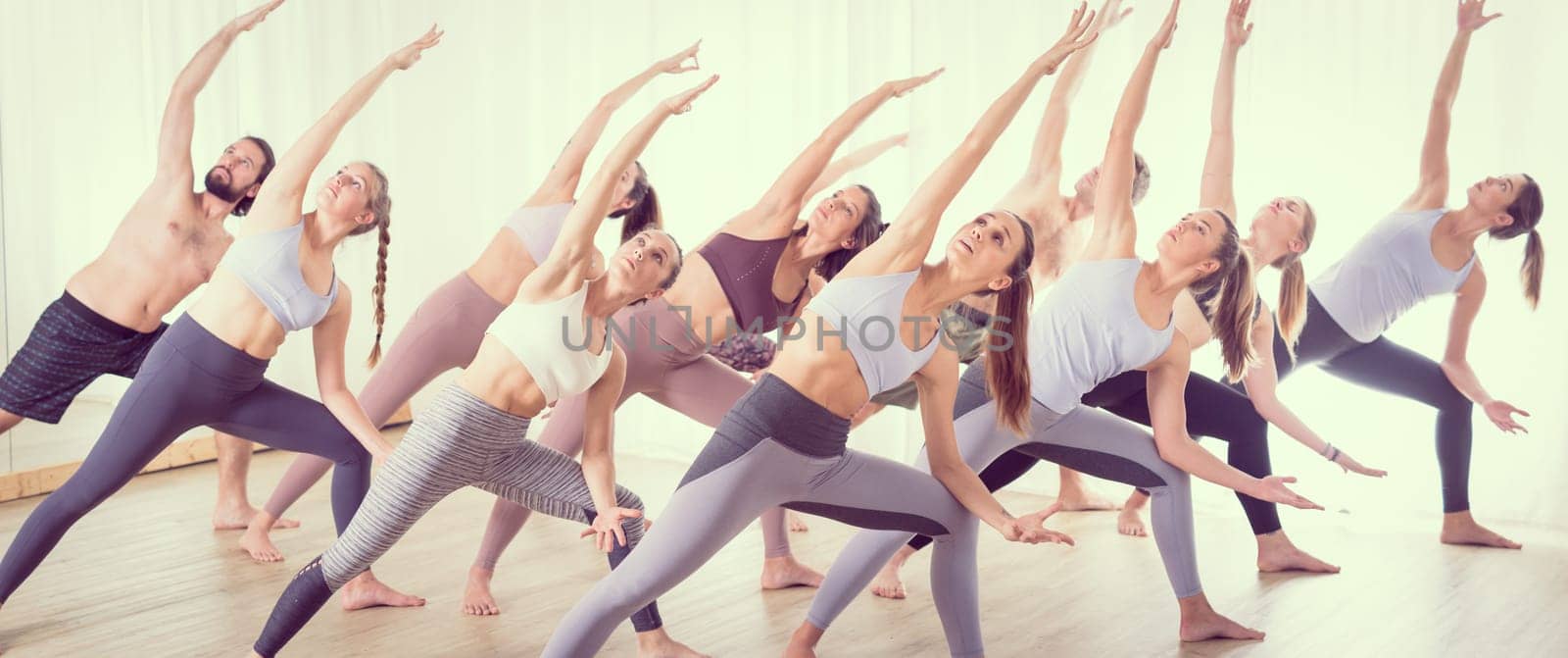 Group of young sporty attractive people in yoga studio, practicing yoga lesson with instructor, sitting on floor in Padmasana, lotus meditative yoga pose. Healthy active lifestyle, working out in gym.