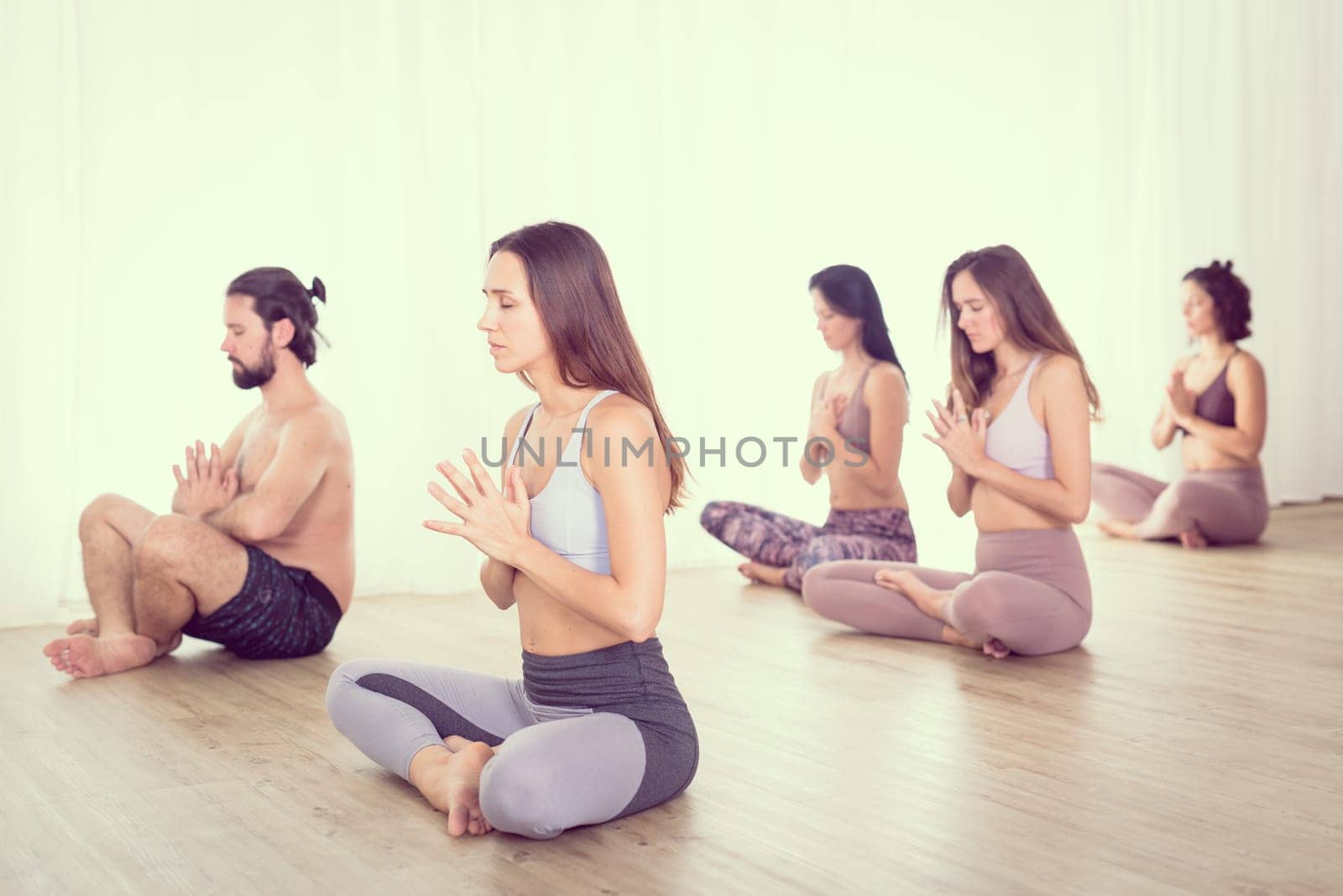 Group of young sporty attractive women in yoga studio, practicing yoga lesson with instructor, stretching and relaxing during workout . Healthy active lifestyle, working out in gym