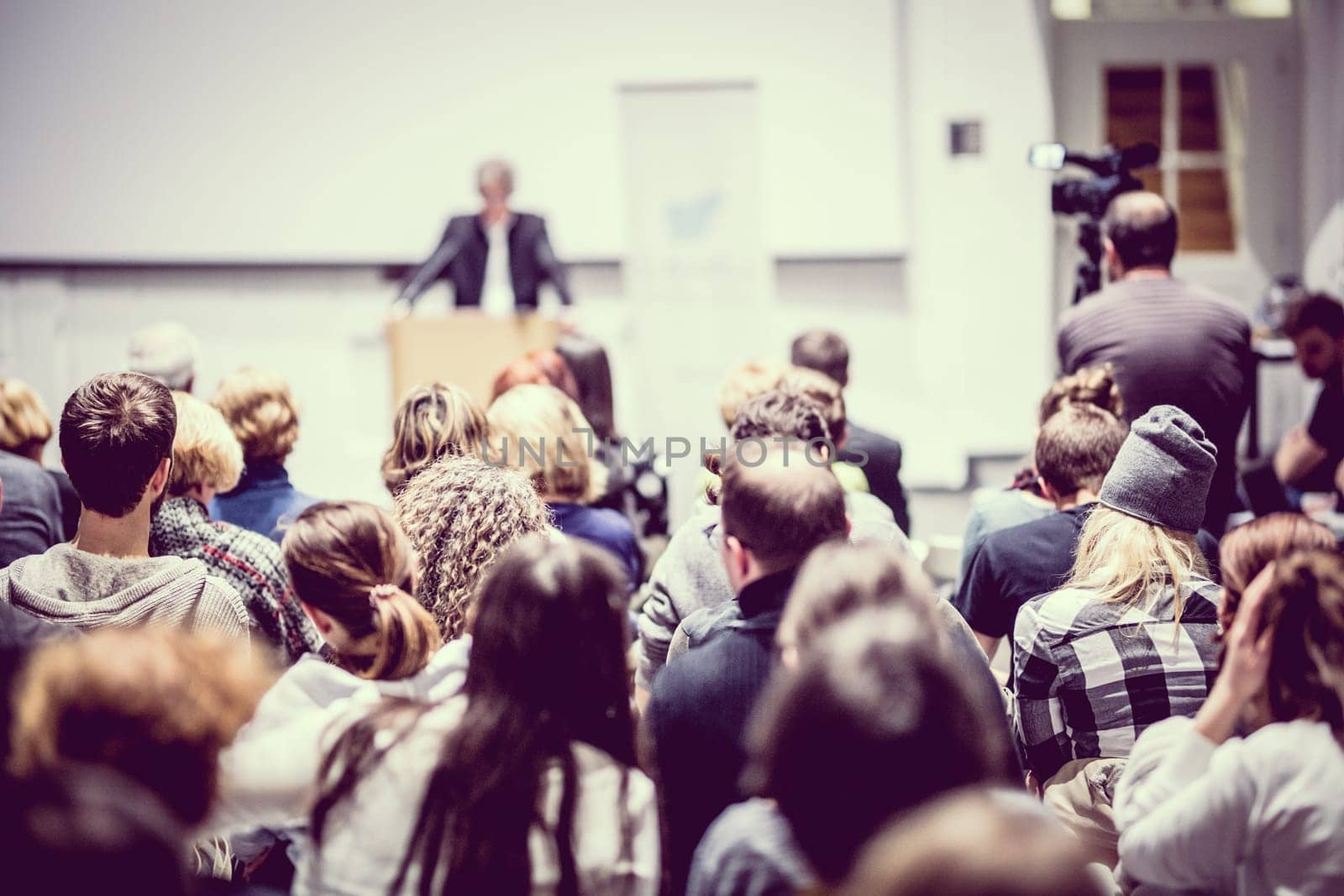 Speaker giving a talk in conference hall at business event. Audience at the conference hall. Business and Entrepreneurship concept. Focus on unrecognizable people in audience.