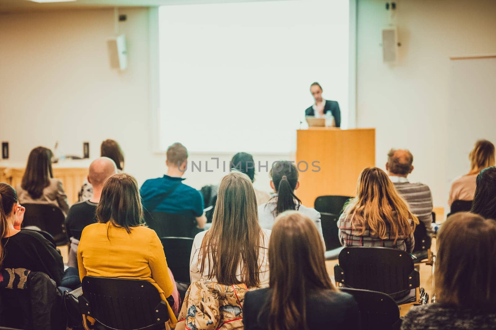 Speaker Giving a Talk at Business Meeting. Audience in the conference hall. Business and Entrepreneurship. Focus on unrecognizable people from rear.