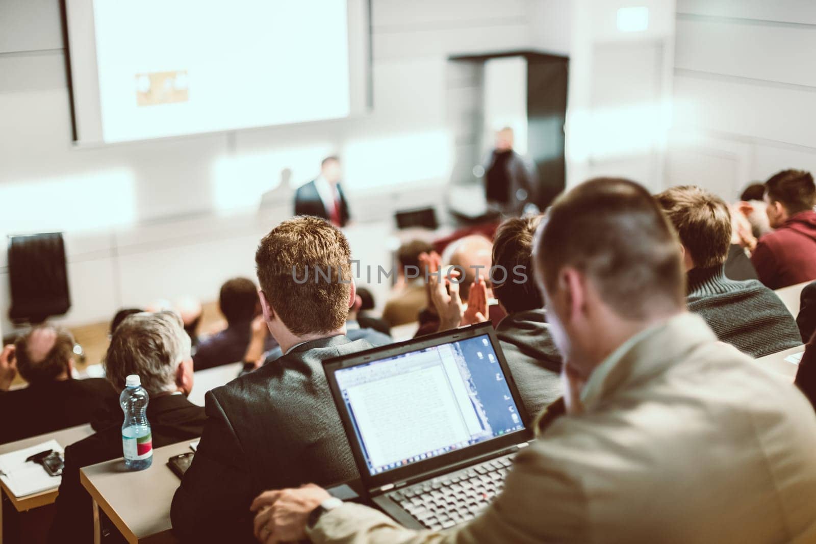 Speaker giving a talk in conference hall at business event. Audience at the conference hall. Business and Entrepreneurship concept. Focus on unrecognizable people in audience.