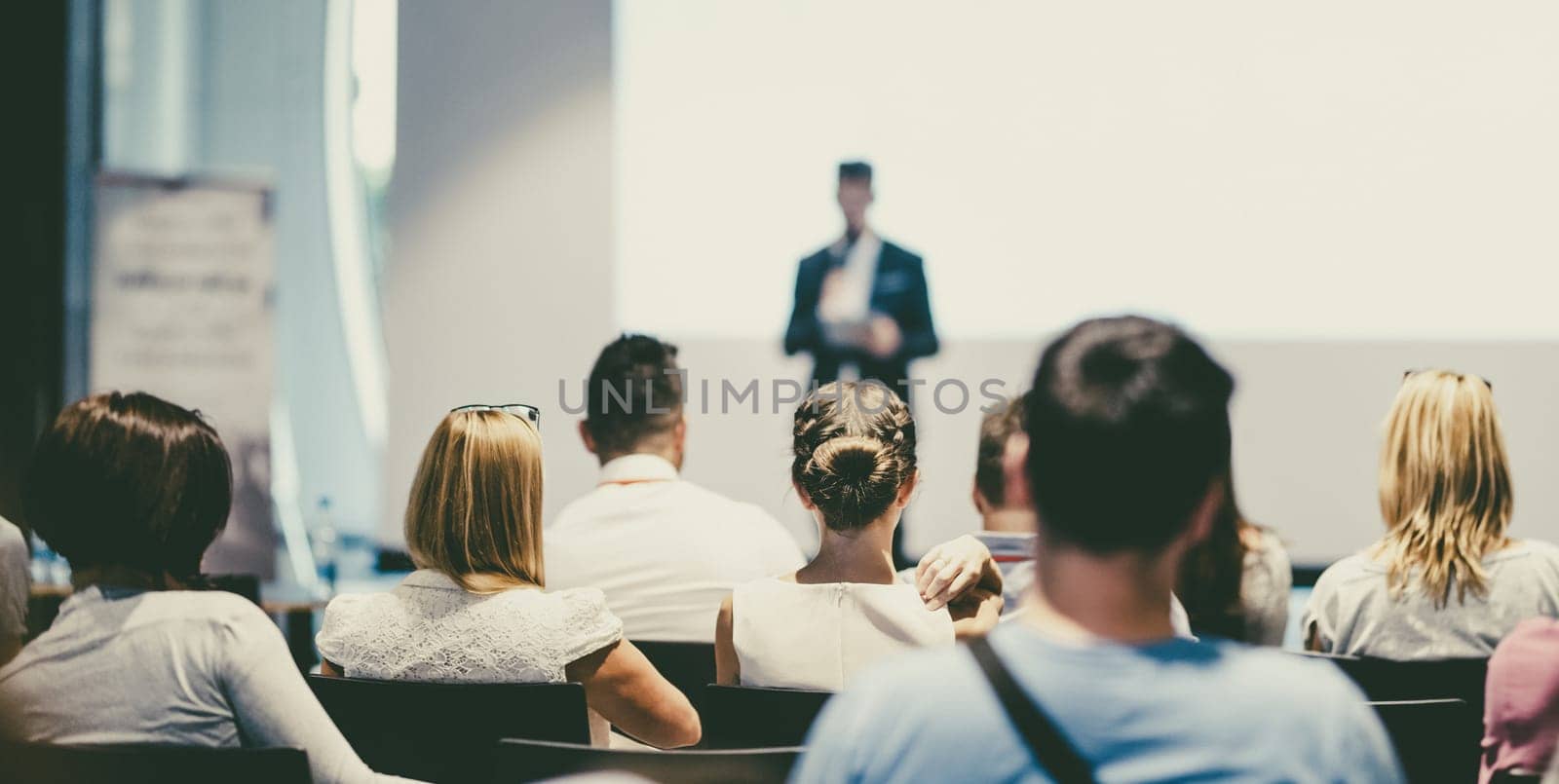 Male speaker giving a talk in conference hall at business event. Audience at the conference hall. Business and Entrepreneurship concept. Focus on unrecognizable people in audience.