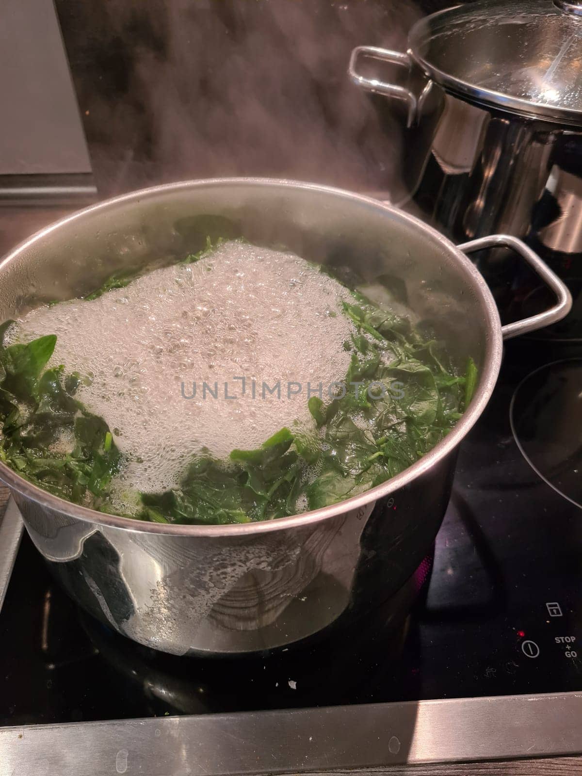 Spinach cooking preparation. Stewed spinach in black cooking pot with spoon on rustic background with ingredients and kitchen utensils . Top view. Home cuisine. Healthy food nutrition