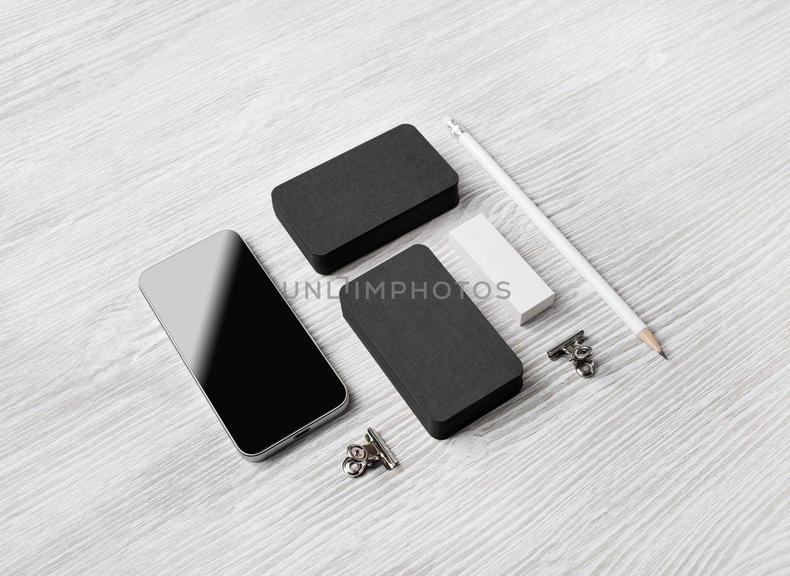 Blank stationery mockup. Blank black business cards, smartphone, pencil and eraser on light wooden background. Brand ID set.