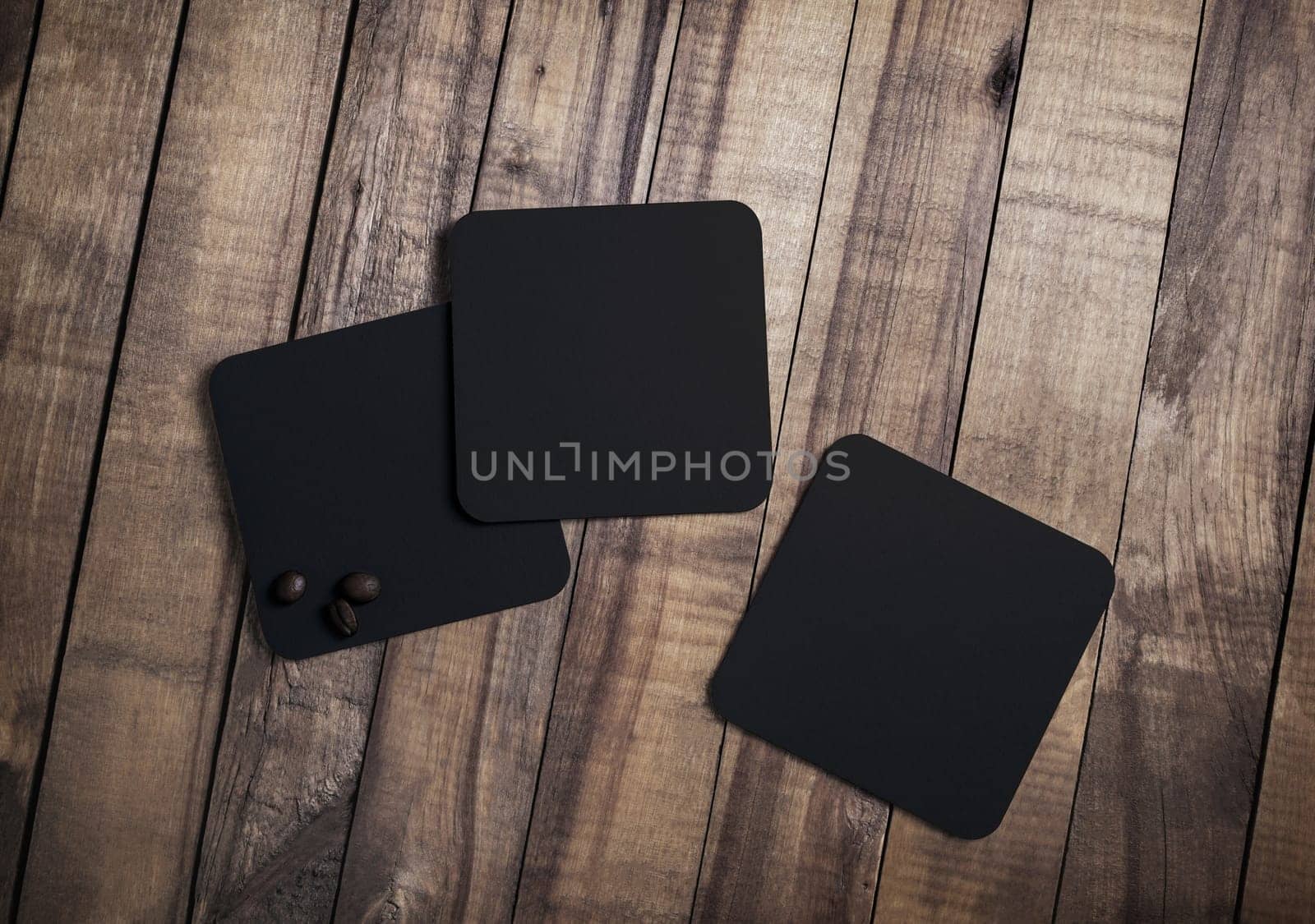 Photo of three blank black square beer coasters and coffee beans on wood table background. Top view. Flat lay.