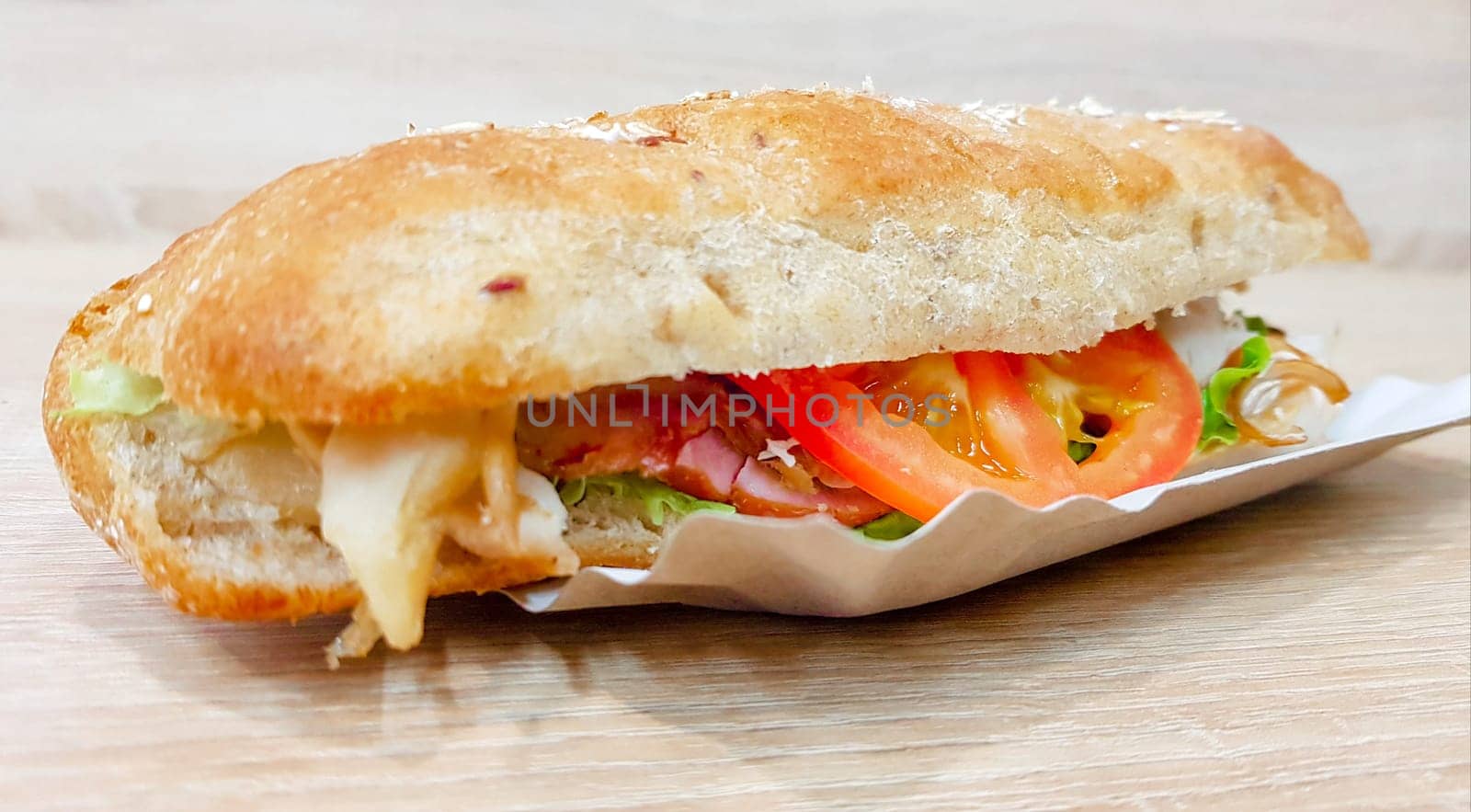 Ciabatta sandwich with lettuce, chicken and cheese on a wooden table.